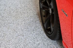 Red sports car parked on a gray flake polyaspartic garage floor coating
